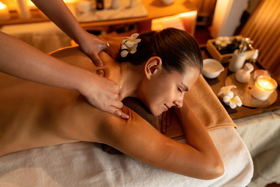 A smiling undressed woman lying face down comfortably with her eyes closed, enjoying a relaxing massage at her back.